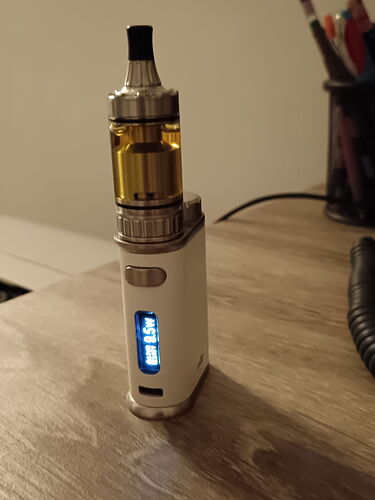 A képen egy fehér színű vaporizátor látható, amelynek az üstje arany színű, és világító kijelzője van. (Feliratozva AI-val)