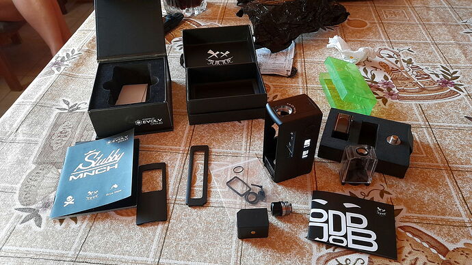 Az asztalon különféle elektronikai eszközök, tartozékok, dobozok és használati útmutatók vannak szétszórva, melyek egy dohányzáshoz kapcsolódó készlet darabjai lehetnek. (Feliratozva AI-val)