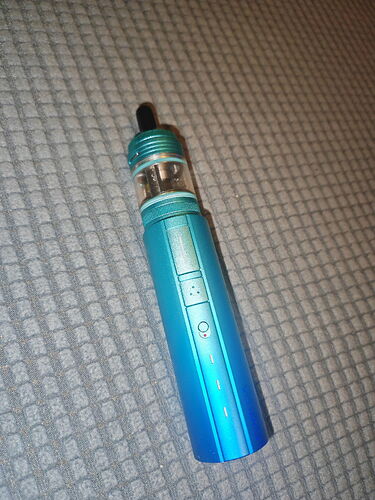 A slim, turquoise-colored e-cigarette lying on a fabric surface. {e-cigarette, vape} (Caption generated by AI)