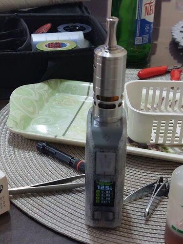 Une cigarette électronique (vape) est posée sur une table, avec divers objets ménagers visibles derrière. (Légendé par l'IA)