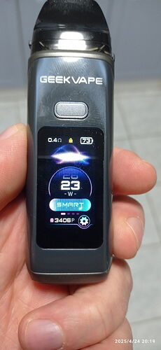 L'image montre une cigarette électronique GEEK VAPE tenue dans la main, dont l'écran numérique affiche divers réglages et données, tels que la puissance (23W) et le niveau de charge de la batterie. (Légendé par IA)