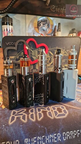 Az asztalon öt különböző kialakítású és színű elektromos cigaretta (vape) eszköz áll egy alátét tetején, amelyen különböző logók és minták láthatók. (Feliratozva AI-val)