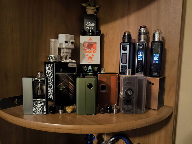 Az image egy fából készült polcon elhelyezett különböző vape eszközöket és tartozékokat mutat be. (Feliratozva AI-val)