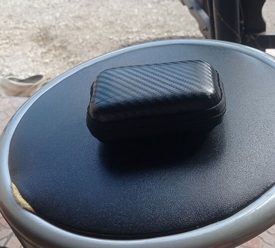 Egy fekete, texturált mintájú tárolódoboz található egy fekete ülőfelületen, amelynek szélén kisebb sérülés látható. (Feliratozva AI-val)