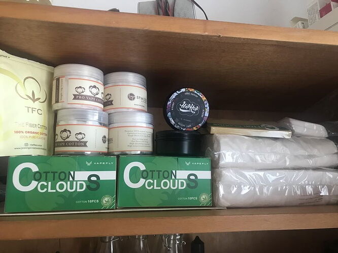 Different wicks and vape products are visible on the shelf, including Pro Vape Cotton, TFC Fiber Cotton, Cotton Clouds boxes, and a HipHop Vape Cotton tank. (Subtitled by AI)
