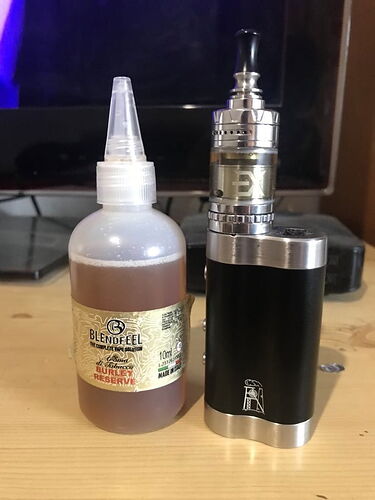 Az asztalon egy folyadékot tartalmazó palack és egy fekete ezüst színű elektromos cigaretta (vape) látható egymás mellett. (Feliratozva AI-val)