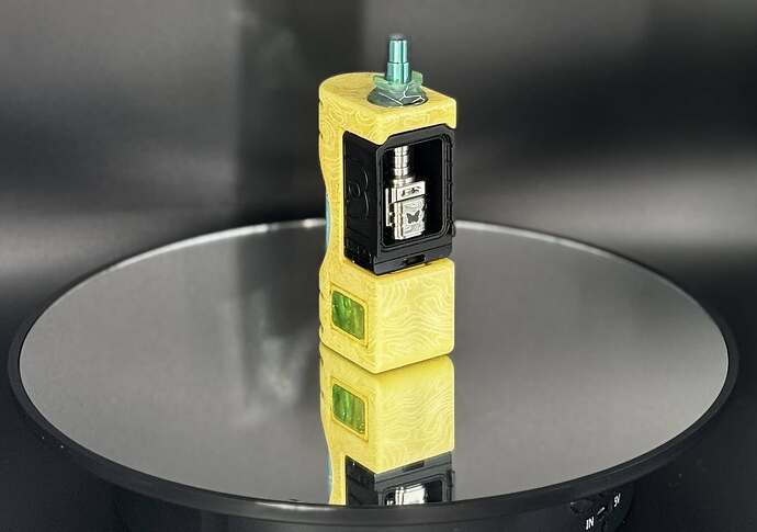 Un appareil de vapotage électrique avec un revêtement extérieur jaune et une structure interne métallique se tient sur une surface réfléchissante. (Étiqueté par IA)