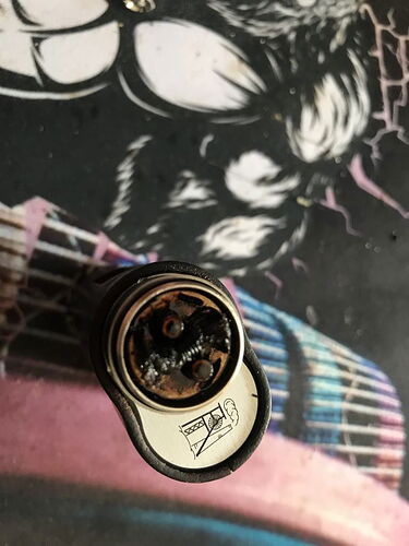 A heavily used and burnt vaporizer or e-cigarette coil head is visible in front of a colorful, illustrated background. (Labeled by AI)