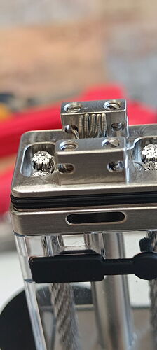 The image shows a close-up photo of a metal component connected by wires and screws, likely part of some electronic or mechanical structure. (AI-generated caption)