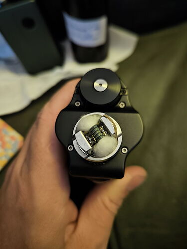 The image shows a black vape device with a dual coil atomizer on top, with white cotton. (AI-captioned)