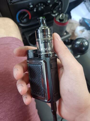 Une main tient un module vape noir et argenté devant le tableau de bord d'une voiture. (Légendé par IA)