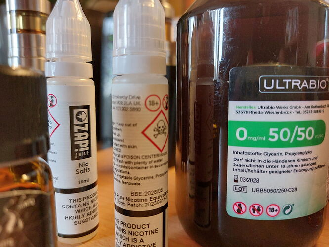 Az képen két nikotintartalmú üveg és egy nagyobb, 50/50-es arányú e-liquid flakon látható, mindegyik vapes használatához. (Feliratozva AI-val)