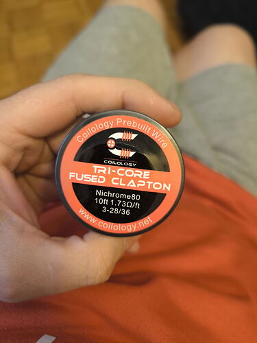 A person holds a jar containing pre-made TRI-CORE FUSED CLAPTON wire of the Coilology brand. (Labeled with AI)