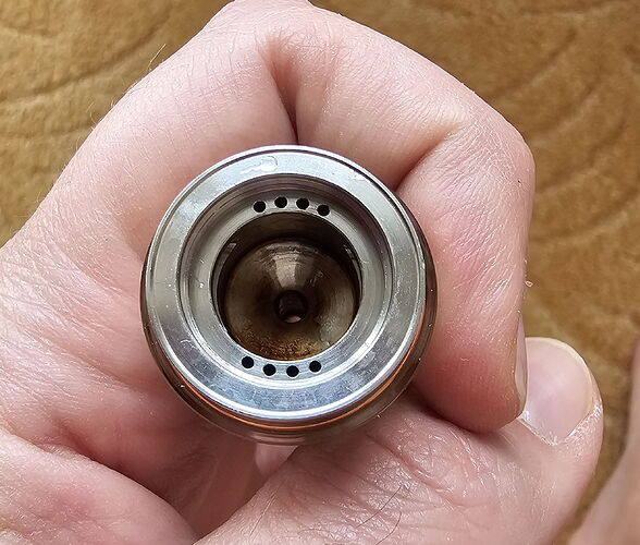 A képen egy fémes szerkezet látható, amelyet egy kéz tart, és a belsejében több kis lyuk található. (Feliratozva AI-val)