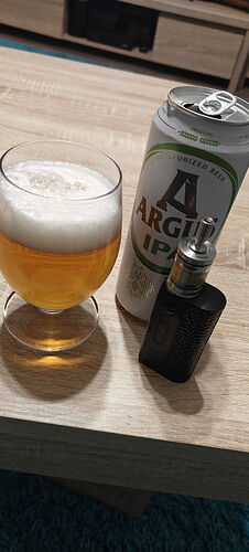 Sur la photo, un verre de bière, une canette de bière et une cigarette électronique sont visibles sur une table en bois. (Légendé par IA)