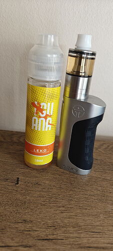 Az asztalon egy e-cigaretta és mellette egy 50 ml-es, sárga színű LEKO ízű e-liquid palack látható. (Feliratozva AI-val)