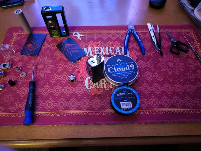 Az asztalon különböző elektronikai és kézi szerszámok, valamint dohányzáshoz használatos kellékek vannak elhelyezve egy piros mintás alátéten. (Feliratozva AI-val)