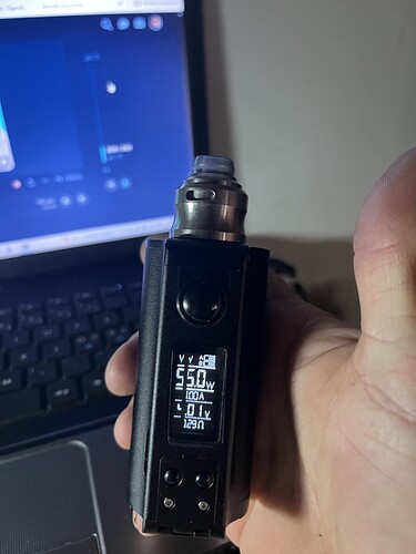 A hand holding a black electronic cigarette, with a laptop with an open screen in the background. (Subtitled by AI)