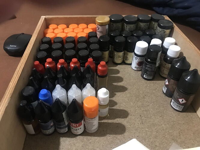 Az képen különböző színű és méretű festékek láthatók egy fa dobozban, rendezetten elhelyezve. (Feliratozva AI-val)