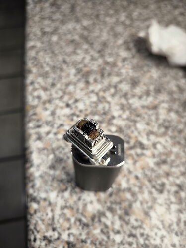 Az image-en egy fém, felnyitott elektromos öngyújtó látható egy kőfelszínű asztalon. (Feliratozva AI-val)