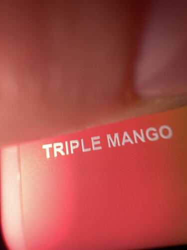 A képen a "TRIPLE MANGO" felirat látható egy vörös háttéren. (Feliratozva AI-val)