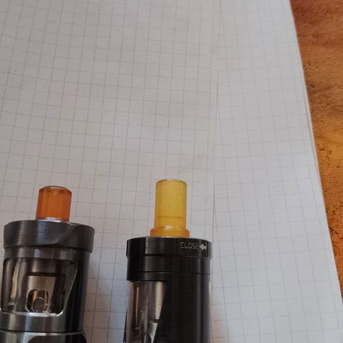 Deux appareils de vape avec des drip tips orange et jaune sont placés sur un papier quadrillé. (Légendé par IA)