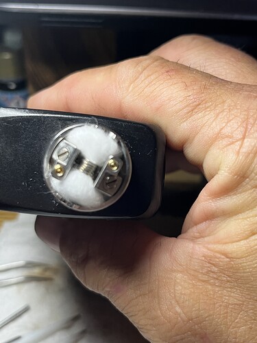 A hand holding an electronic cigarette coil with cotton wick inserted. (Captioned by AI)