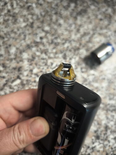 A hand holds a disassembled, electronically regulated vape mod, showing its heating wire and atomizer head. (AI-generated caption)