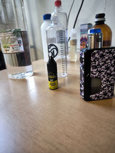 Sur la table se trouvent divers flacons, un flacon distributeur de liquide et une boîte à motifs noirs. (Légendé par IA)