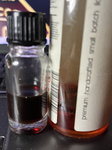 In the picture, a small bottle with dark liquid and behind it a larger bottle is visible, whose label reads 'premium handcrafted small batch'. (Captioned by AI)