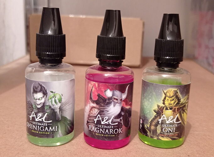 A képen három különböző színű és címkéjű A&L Ultimate e-liquid üveg látható, amelyek közül a címkék Shinigami, Ragnarok és Oni karaktereket ábrázolnak. (Feliratozva AI-val)