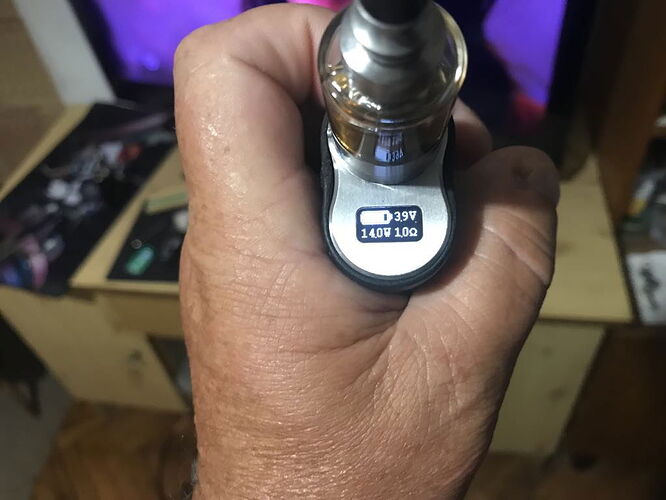 The image shows an e-cigarette held in a hand, on which the display shows the battery charge, the wattage, and the resistance value. (Labeled by AI)
