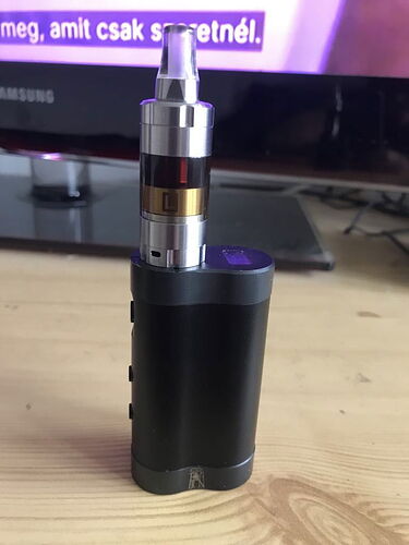 A black electronic cigarette stands on a table in front of a TV displaying Hungarian text. (Subtitled with AI)