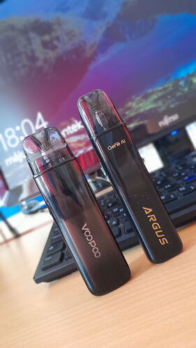 Two black electronic smoking devices (Voopoo and Argus) stand on a table in front of a computer keyboard. (Labeled with AI)