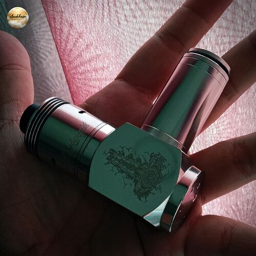 Une main tient un mod vape en métal avec un design décoré, devant un fond rose. (Légendé par IA)