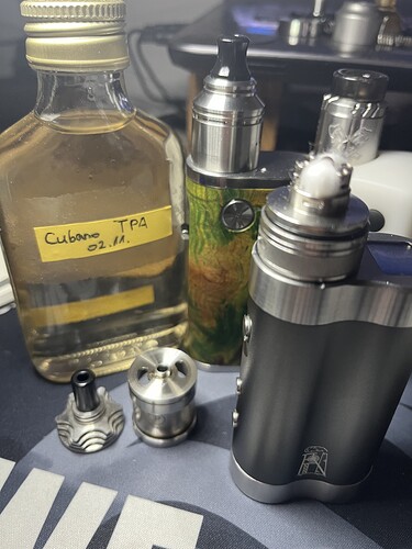 Az изображение egy asztalon lévő vape eszközöket és egy üveg folyadékot ábrázol, amelyen a "Cubano TPA" felirat látható. (Feliratozva AI-val)