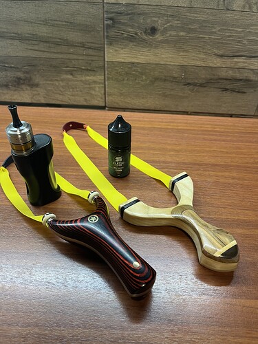 Sur la table, on voit deux lance-pierres à manche en bois et une cigarette électronique avec une petite bouteille. (Légendé par IA)