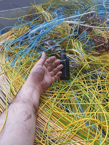 A human hand reaches for a black walkie-talkie amidst many colorful, mainly yellow and blue cables. (Captioned by AI)