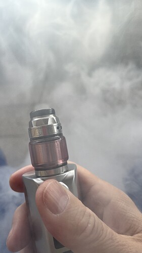 A hand holds a metallic-colored vape device, from which a large amount of vapor rises. (Labeled by AI)