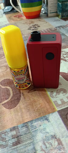 A bottle of liquid with a yellow plastic cap and an electronic device with a red and black button are placed next to each other on a table. (Annotated by AI)