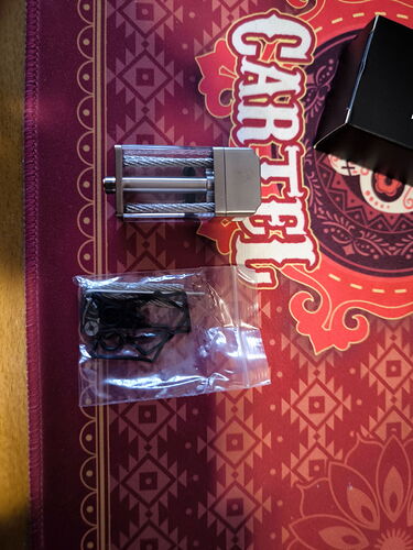 A metal device and a black object in a transparent bag are shown in the image, all placed on a red and patterned mat. (Autogenerated by AI)