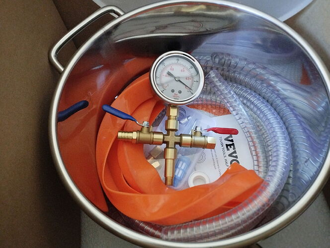 Un assemblage avec un manomètre et des tuyaux, ainsi qu'un tuyau orange, se trouve à l'intérieur d'un seau en métal. (Légendé par IA)