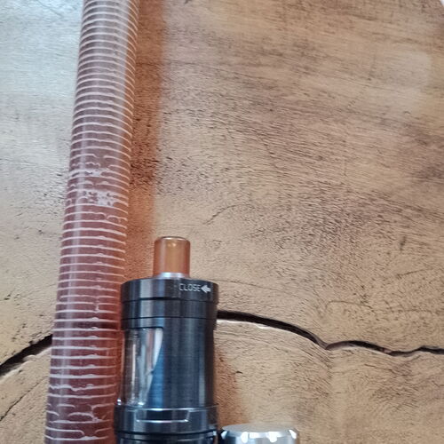 Un appareil de vapotage de couleur foncée avec un drip tip couleur ambre et un tube transparent côtelé reposent sur une surface en bois. (Légendé par l'IA)