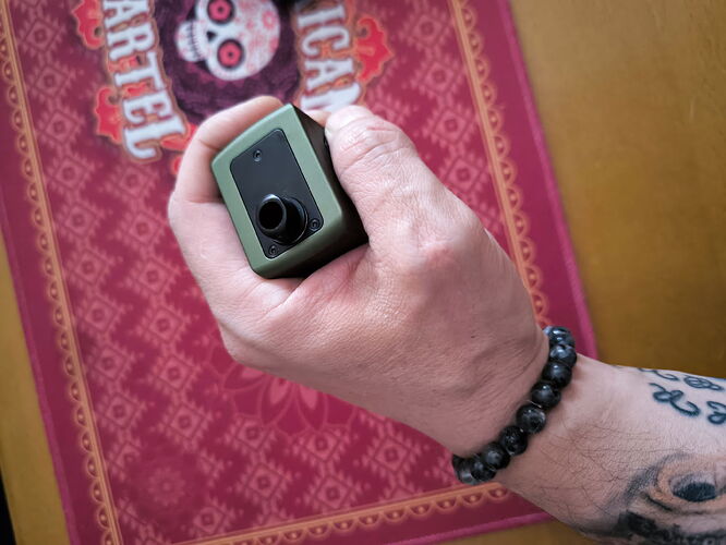 A human hand is shown holding a green device in the image, with a beaded bracelet and a decorative background. (Autogenerated by AI)