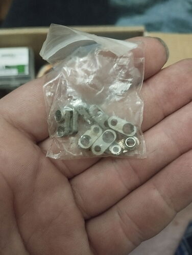 Une main tient un petit sac en plastique transparent contenant plusieurs petites connecteurs métalliques ou extrémités de câble. (Étiqueté par l'IA)