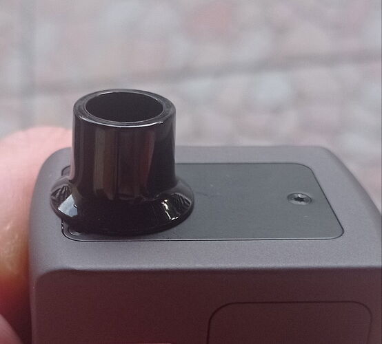 Egy kéz tart egy fekete kütyüt, amelyen egy fekete, hengeres nyílás található. (Feliratozva AI-val)