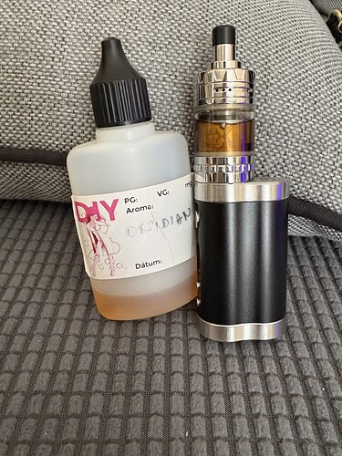 In the picture, an e-cigarette and a DIY bottle containing liquid are visible, placed on a gray surface. (Labeled by AI)