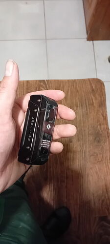 A hand holds a black, compact electronic cigarette (vape) over a wooden table. (Labeled by AI)