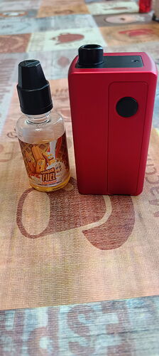A red electronic cigarette device and a bottle of flavored liquid are on a patterned tablecloth. (AI-generated caption)