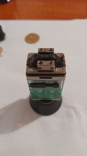 An electronic cigarette or vape component with burnt residue on top, resting on a white surface. (Subtitled by AI)